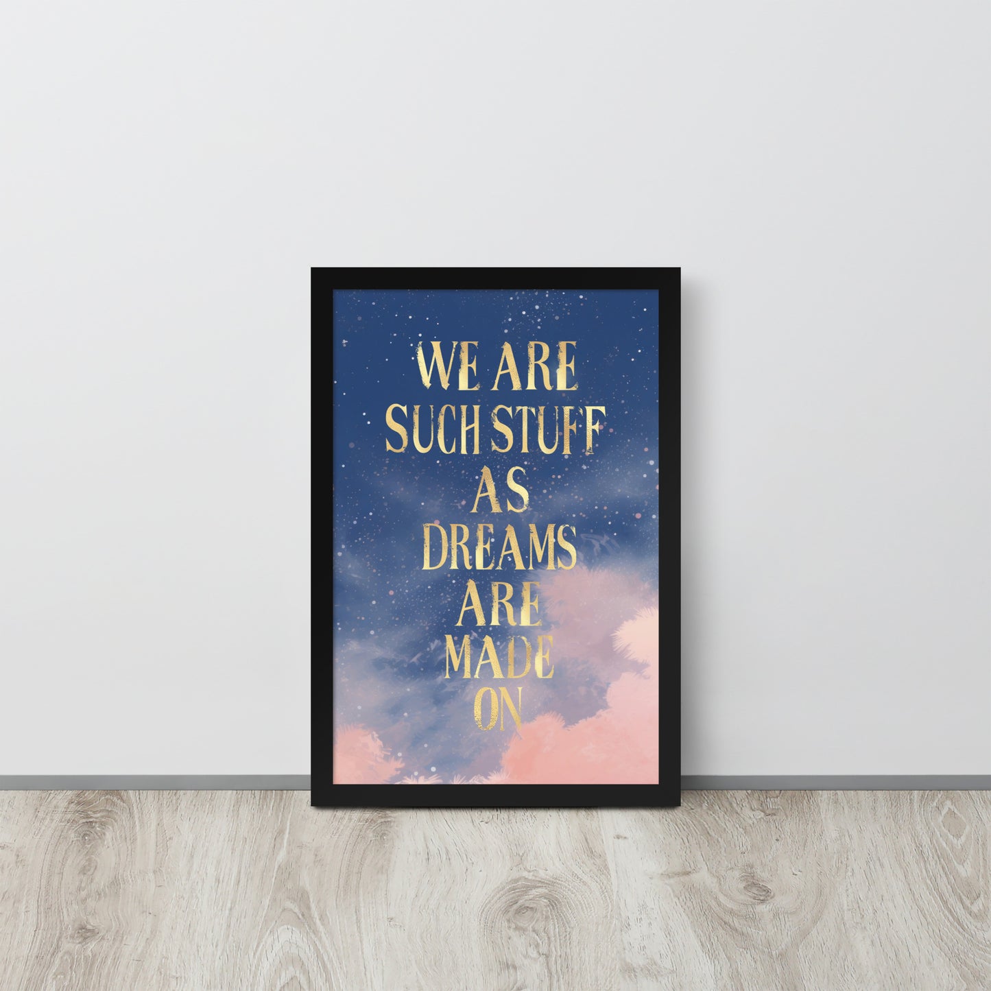 black Framed wall art print with gold text reading “We are such stuff as dreams are made on” over a dreamy starry night sky with pink clouds against white wall
