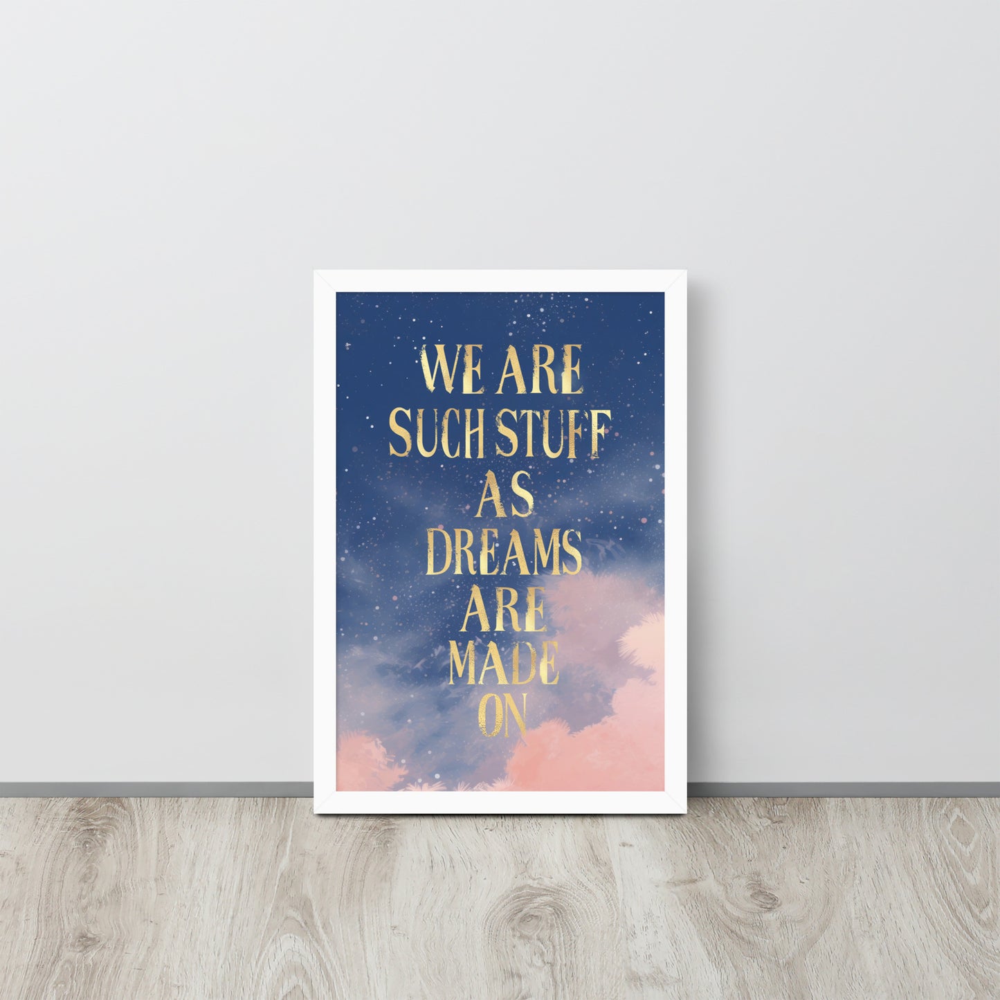 white Framed wall art print with gold text reading “We are such stuff as dreams are made on” over a dreamy starry night sky with pink clouds, against a white wall