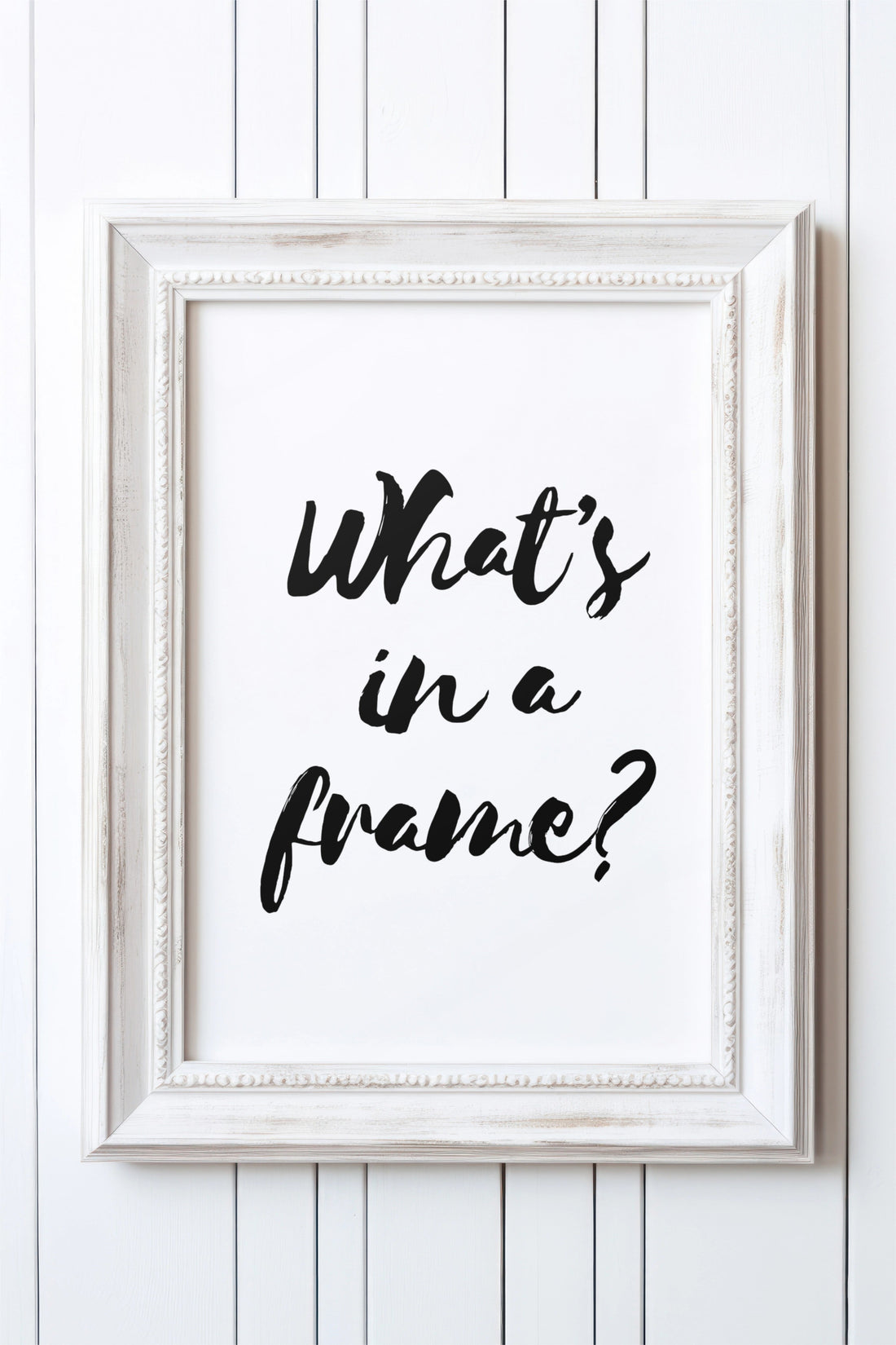 Distressed white wooden frame on a white panelled wall, displaying a black brush-script print that reads "What's in a frame?